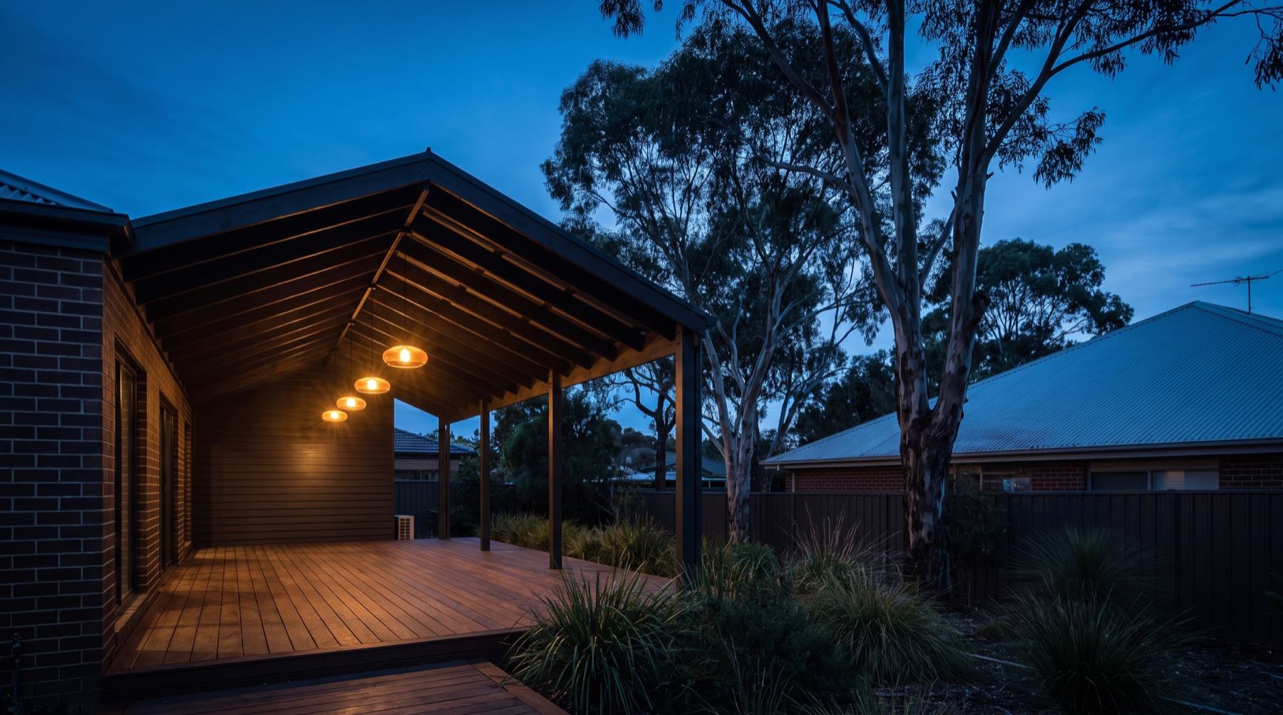 A covered timber patio at the back of a house lit from beneath at dusk
