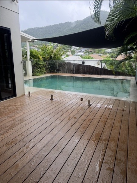 A timber pool deck with a glass balustrade after rain