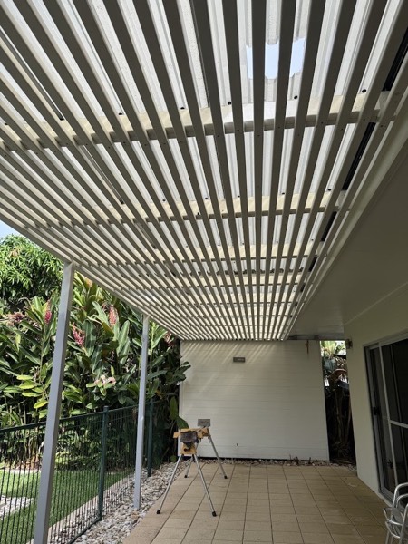 A slatted timber patio roof over a paved area beside a house