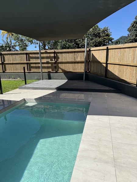 A timber deck beside a swimming pool under a shade sail