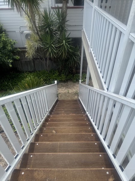Timber steps and a landing with a white balustrade beside a house