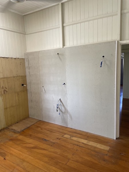 An interior room mid-renovation with timber flooring and a stripped wall