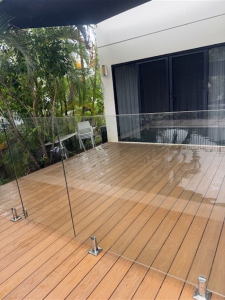 A timber deck with a glass balustrade beside sliding doors after rain
