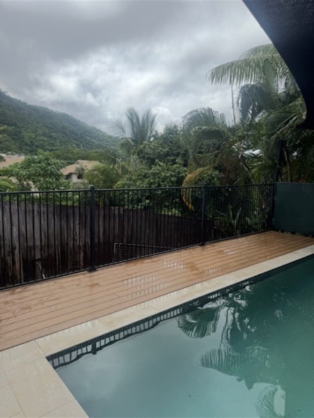 A timber deck running along the edge of a swimming pool behind a dark fence