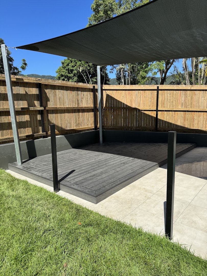 A timber deck under a shade sail next to a paling fence and lawn